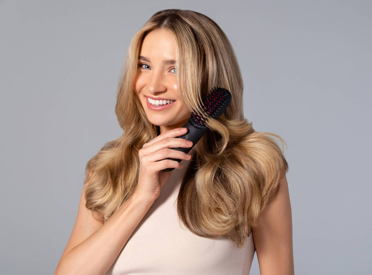 A woman with golden locks smiles as she gently brushes through her hair with a TYMO brush, showcasing the grace of effortless styling.
